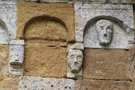Teste umane scolpite sul muro della Badia a Coneo: i guardiani della soglia